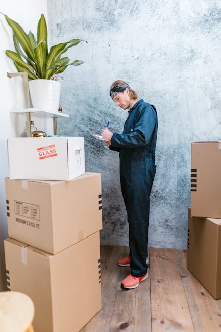 A professional removalist from removaloffice.com is inside a residential property preparing for a home relocation. He is holding a clipboard and using a pen to check inventory or plan the packing proc